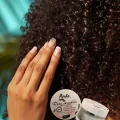 Femme aux cheveux texturés appliquant le Baume Universel Pipeska pour définir les boucles et sceller l'hydratation. Baume Universel Bio & 100% Naturel | Soin Visage, Corps, Cheveux | Pipeska